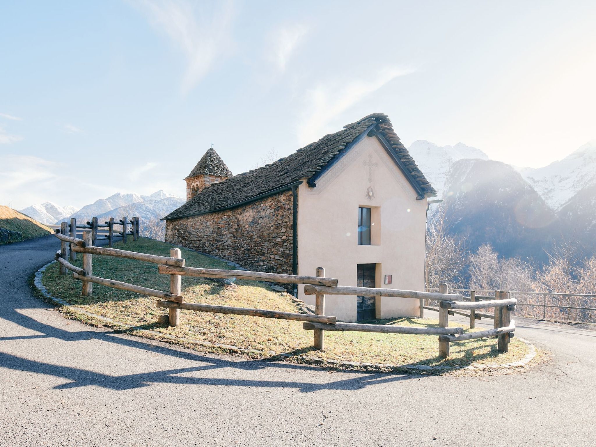 A small stone building with a wooden fence in front, surrounded by a mountainous landscape.