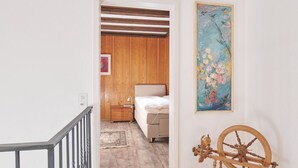 A bedroom with a bed, a nightstand, a painting, and a wooden spinning wheel. - Casa Bubeck by Interhome (Sobrio)