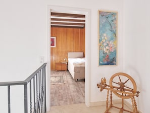 A bedroom with a bed, a nightstand, a painting, and a wooden spinning wheel. - Casa Bubeck by Interhome (Sobrio)