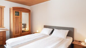 A double bed with white linens, a wooden wardrobe, and bedside lamps. - Casa Bubeck by Interhome (Sobrio)