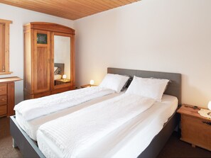 A double bed with white linens, a wooden wardrobe, and bedside lamps. - Casa Bubeck by Interhome (Sobrio)