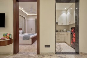 A modern bedroom with a bed, a bedside table with snacks, and a bathroom with a shower. - Hotel Golden Place 325E (Gurugram)