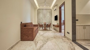 Una sala de estar moderna con un sofá marrón, una mesa de comedor y sillas. Hay un televisor montado en la pared y una zona de cocina con armarios.