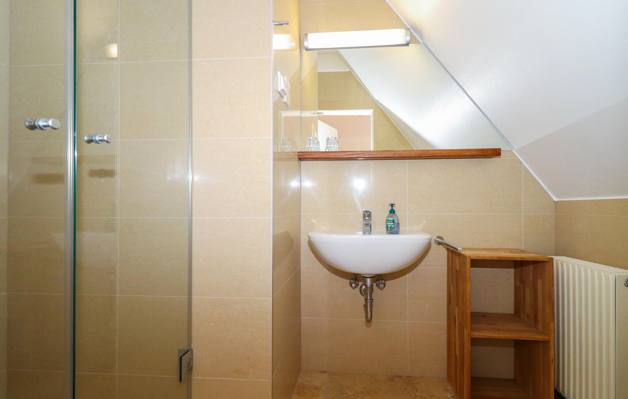 Un baño con cabina de ducha de vidrio, un lavamanos blanco con estante de madera encima y un radiador en el suelo.