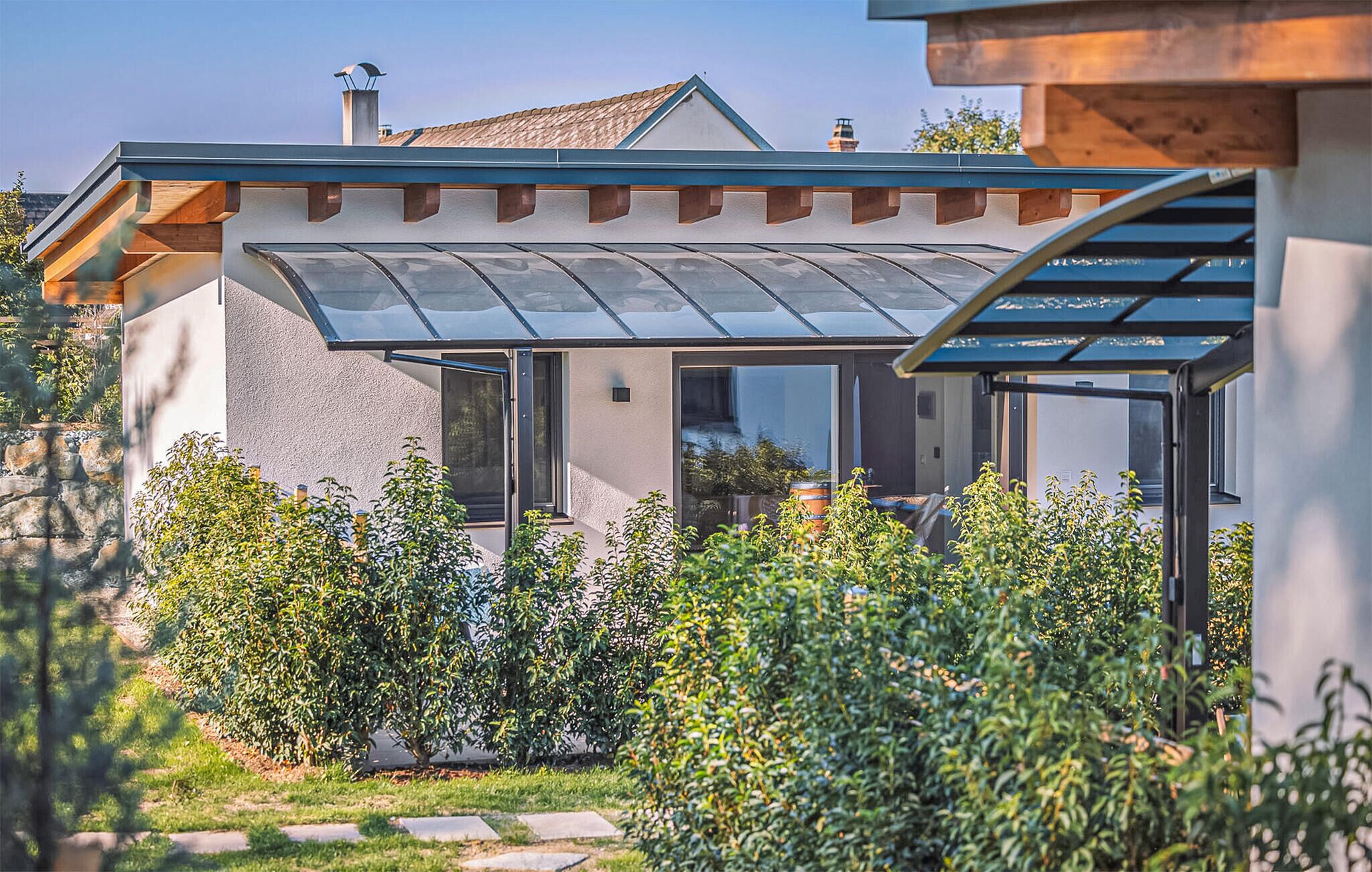 A modern house with a glass conservatory, stone pathway, and lush greenery.