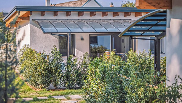 Et moderne hus med et glaskonservatorium, en stensti og frodig vegetation.