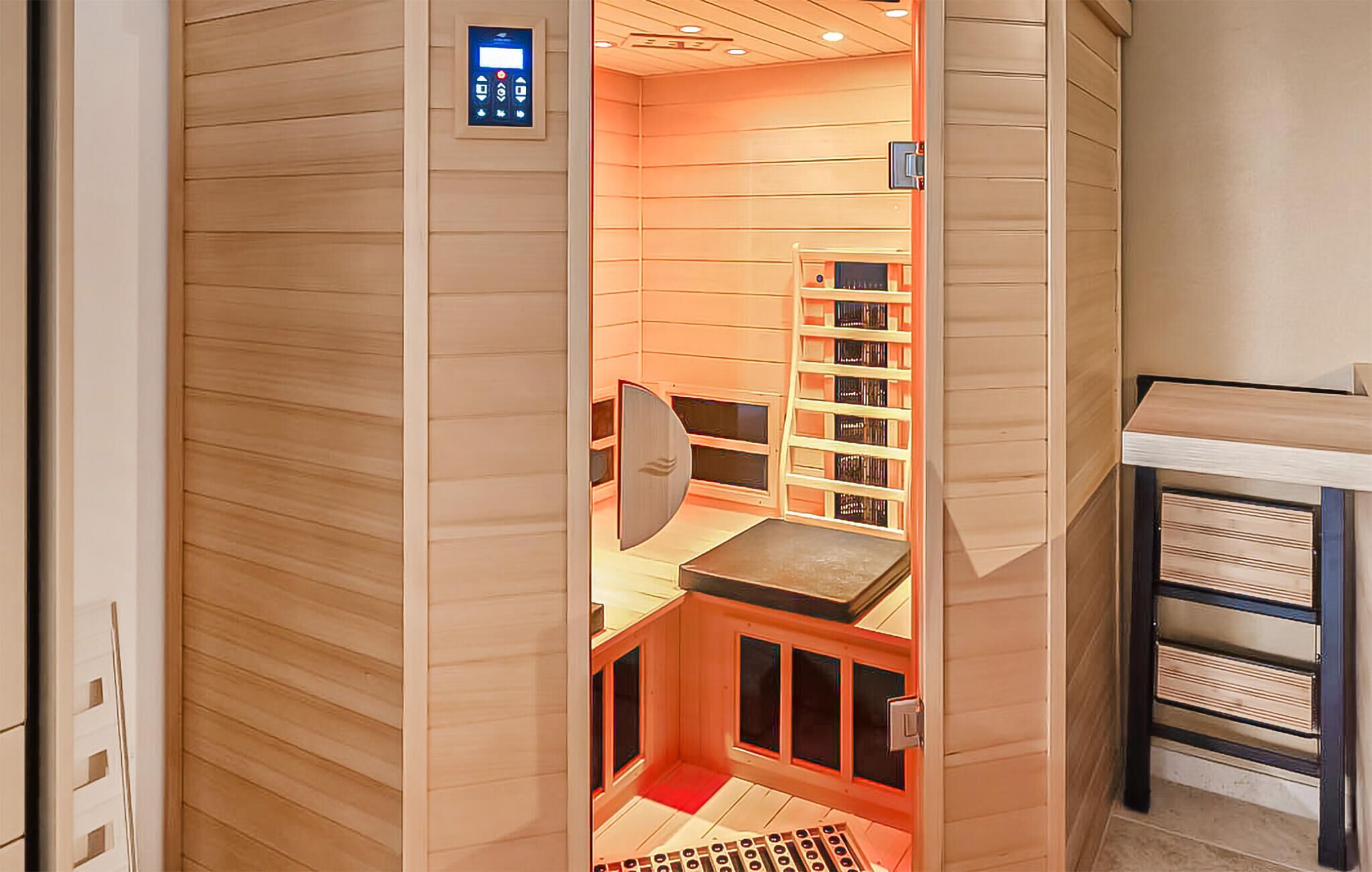 A sauna room with a control panel, a wooden bench, and a bookshelf.