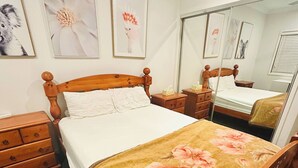 A bedroom with a wooden bed, a bedside table, a dresser, and a mirror. - Room-cozy Room Rental in Caloundra West (Sunshine Coast)