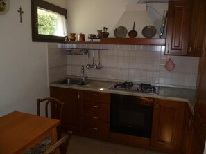 A kitchen with wooden cabinets, a sink, a stove, and various kitchen utensils. - Nido del Tadini' Wohnung mit Parkplatz by Interhome (Lovere)