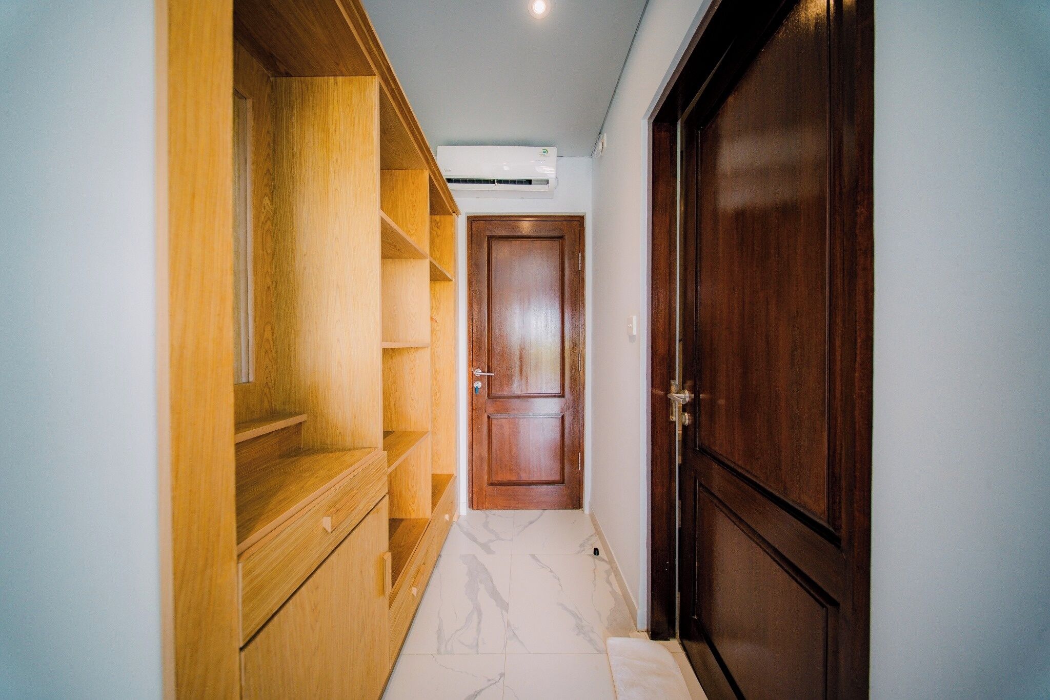 Un pasillo con un armario de madera, piso de mármol y una puerta de madera cerrada.