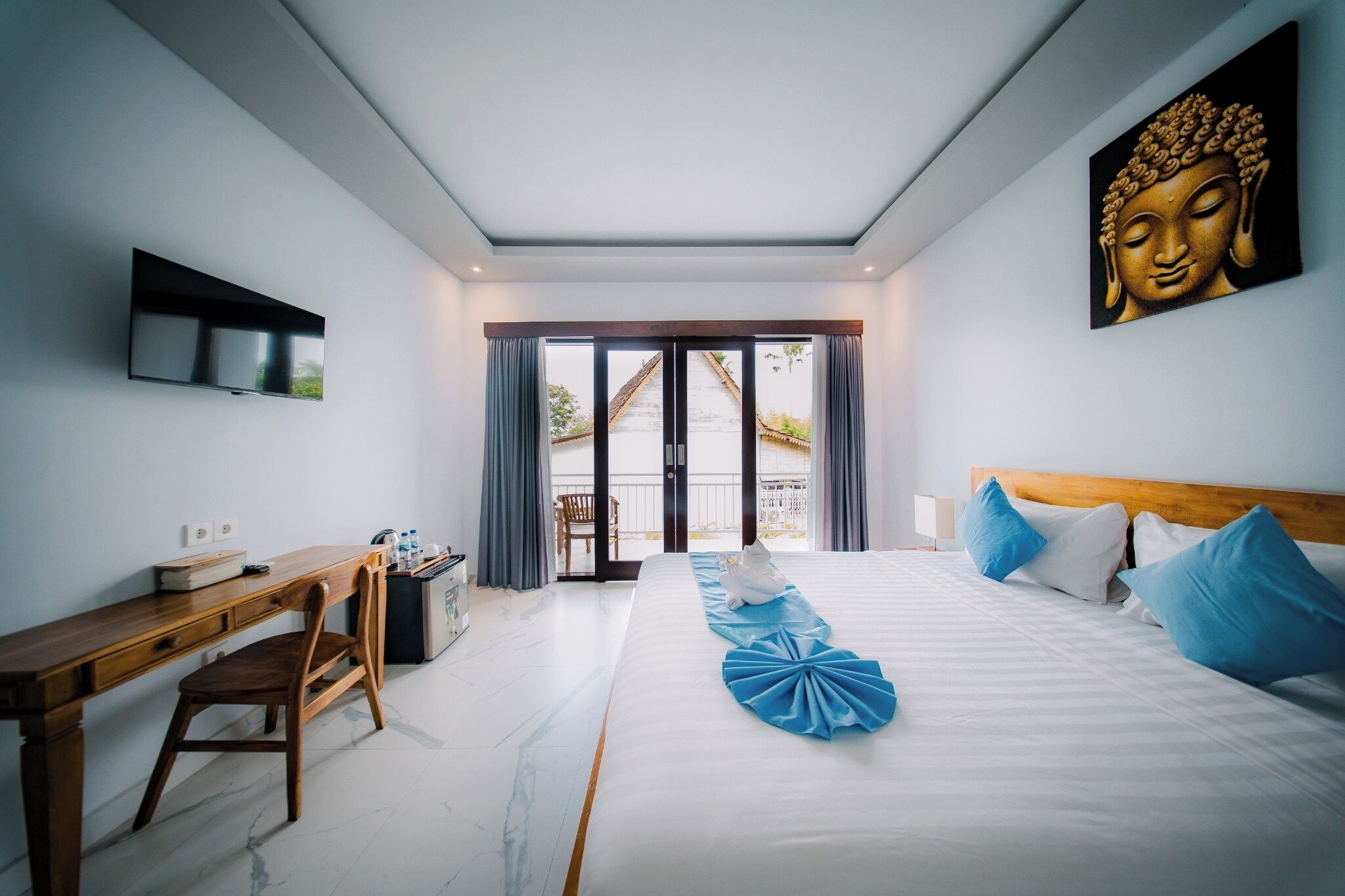 Une chambre d’hôtel équipée d’un lit, d’un bureau, d’une chaise, d’une télévision et d’un tableau représentant un Bouddha.