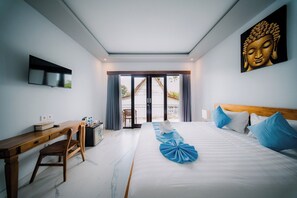 A hotel room with a bed, a desk, a chair, a television, and a Buddha painting. - Puspa Guest House (Pererenan)