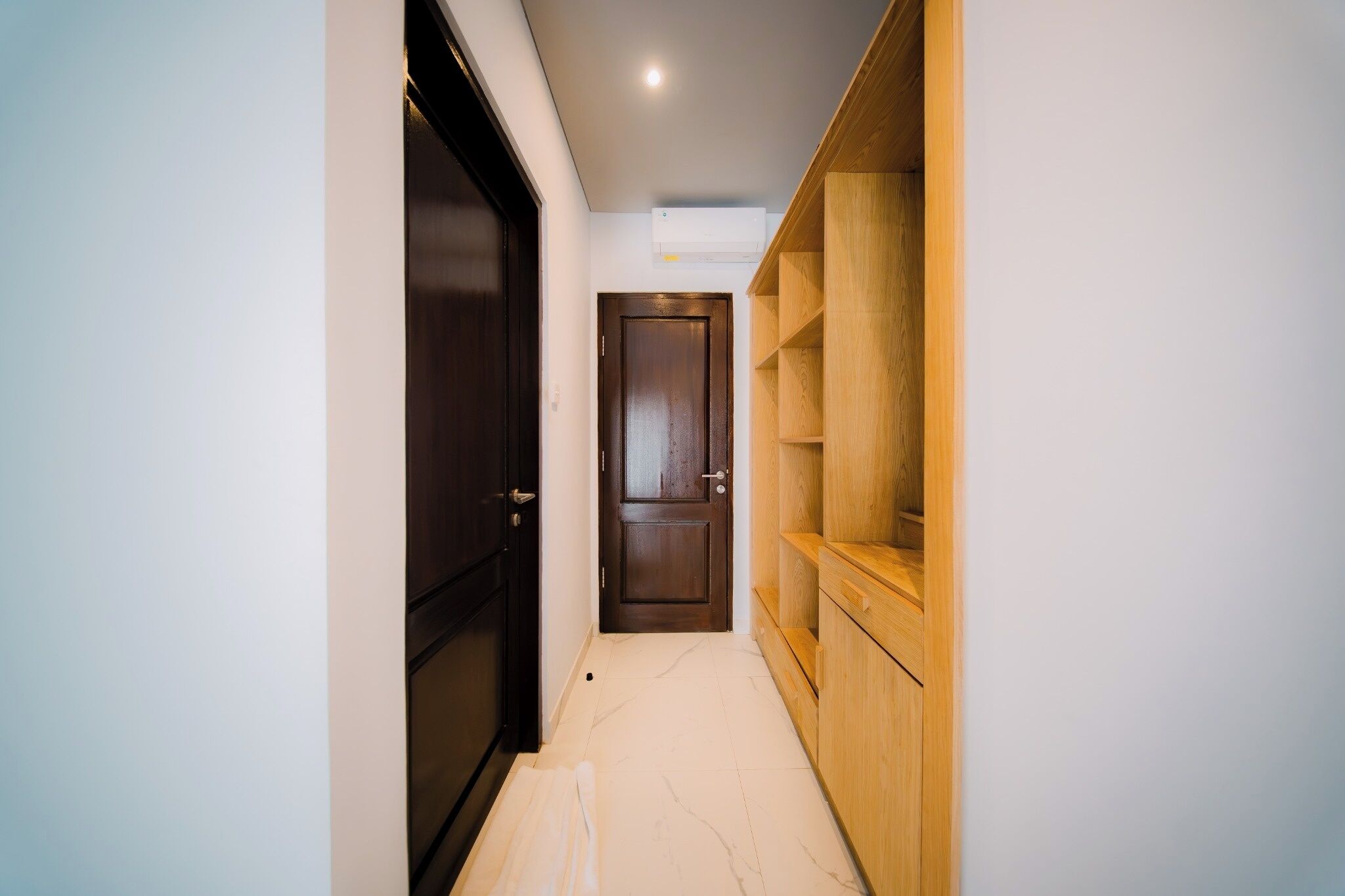 A hallway with a dark wooden door, a white wall, and a wooden shelving unit.
