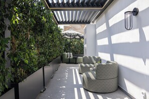 A modern outdoor seating area with a sofa and chairs, surrounded by greenery and a pergola. - Exclusive Serviced Penthouse in Kolonaki (Athens)