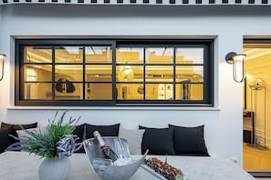 A modern interior with a large window, a dining area with a table set for two, and a potted plant. - Exclusive Serviced Penthouse in Kolonaki (Athens)