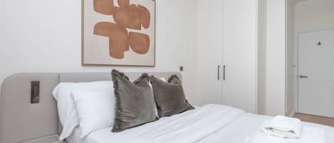 Quarto com cama, almofadas, mesa de cabeceira, uma obra de arte na parede e um guarda-roupa.