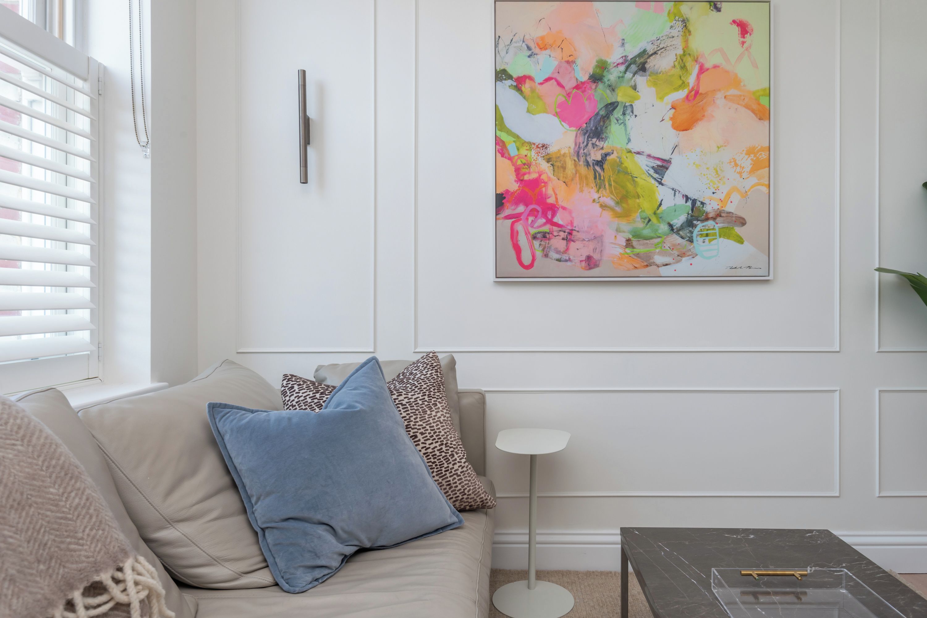 Un salon avec un canapé beige, un coussin bleu, un coussin à motifs léopard, une lampe sur pied et une table basse en marbre.