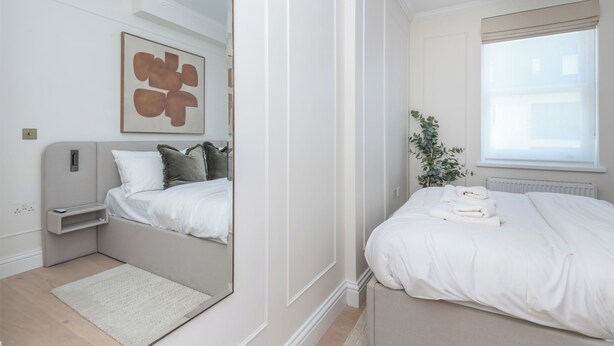 A modern bedroom with a bed, bedside table, and a large mirror. - Modern 2BDR with Workspace in Clapham Junction (Greater London)
