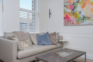 Un salon moderne avec un canapé beige, une table basse en verre et un tableau abstrait aux couleurs vives accroché au mur.