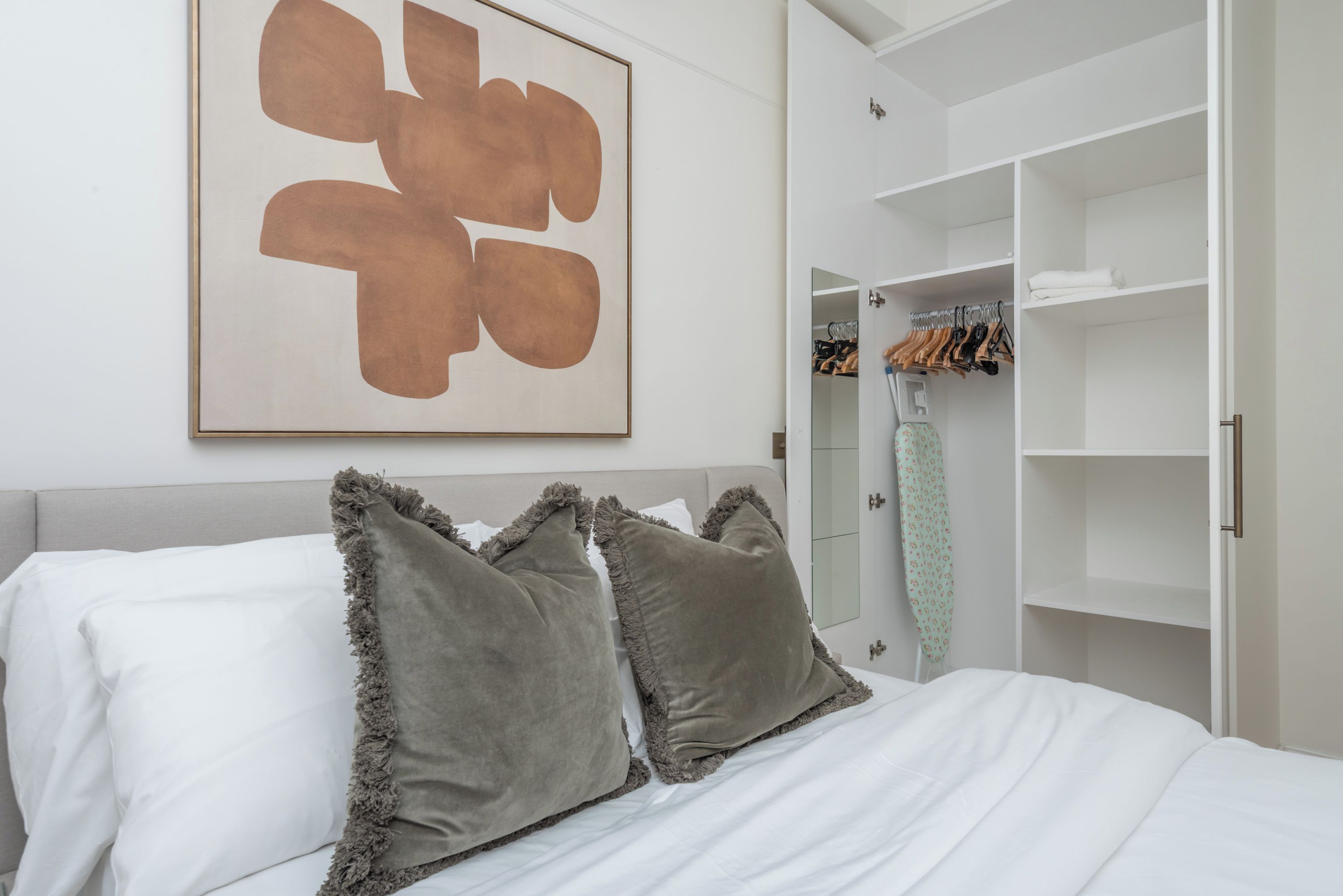 A bedroom with a bed, a wardrobe, and a large abstract painting on the wall.