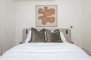Une chambre d’hôtel avec un lit, deux tables de chevet, une œuvre d’art accrochée au mur et un design simple et épuré.