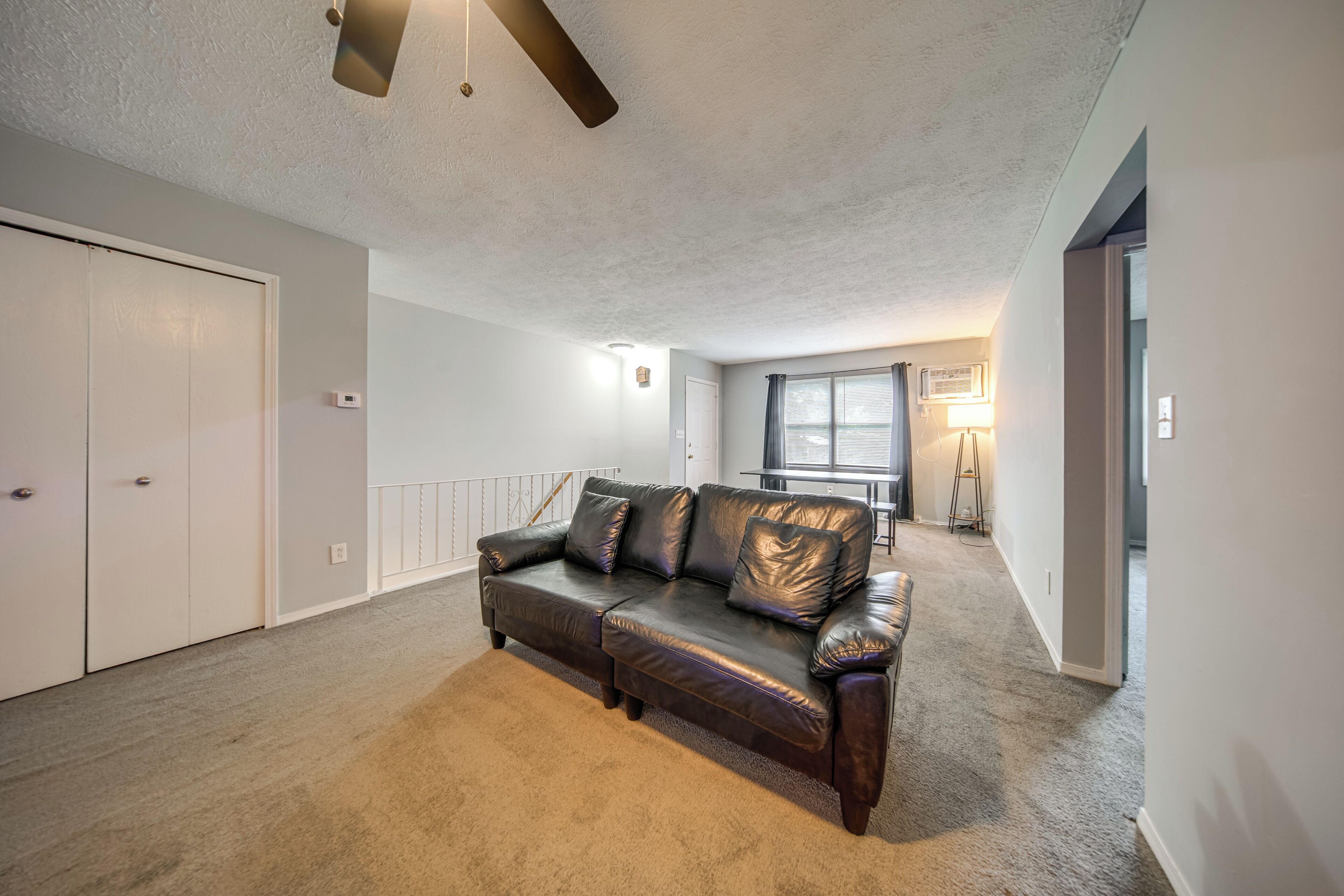 A spacious living area with a leather sofa, a ceiling fan, and a view of the outdoors through a window.