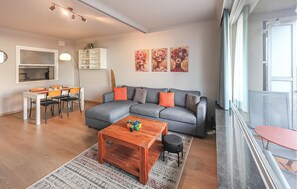 Ein modernes Wohnzimmer mit einem grauen Sofa, einem Holztisch und einem Essbereich mit weißem Tisch und Stühlen.