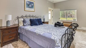 A bedroom with a bed, bedside tables, a lamp, a framed picture on the wall, and a window with a view of trees. - Luxury Forest Retreat: Movie Room, Games, Hot Tub (Colorado Springs)