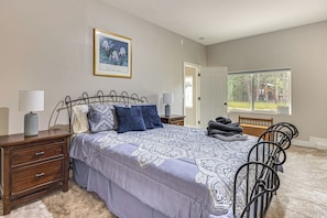 A bedroom with a bed, bedside tables, a lamp, a framed picture on the wall, and a window with a view of trees. - Luxury Forest Retreat: Movie Room, Games, Hot Tub (Colorado Springs)