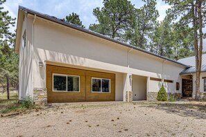 A modern two-story house with a large garage door, a stone foundation, and a well-maintained lawn. - Luxury Forest Retreat: Movie Room, Games, Hot Tub (Colorado Springs)