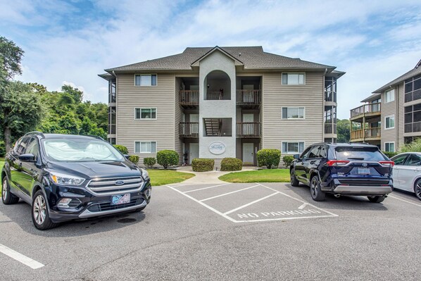A multi-story apartment building with a central entrance, parking spaces, and a clear sky. - Lake-View Balcony, Pool Access! Sunset Beach Condo (Sunset Beach)