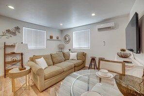 Ein modernes Wohnzimmer mit einem beigefarbenen Sofa, einem Glastisch und einem an der Wand befestigten Flachbildfernseher.
