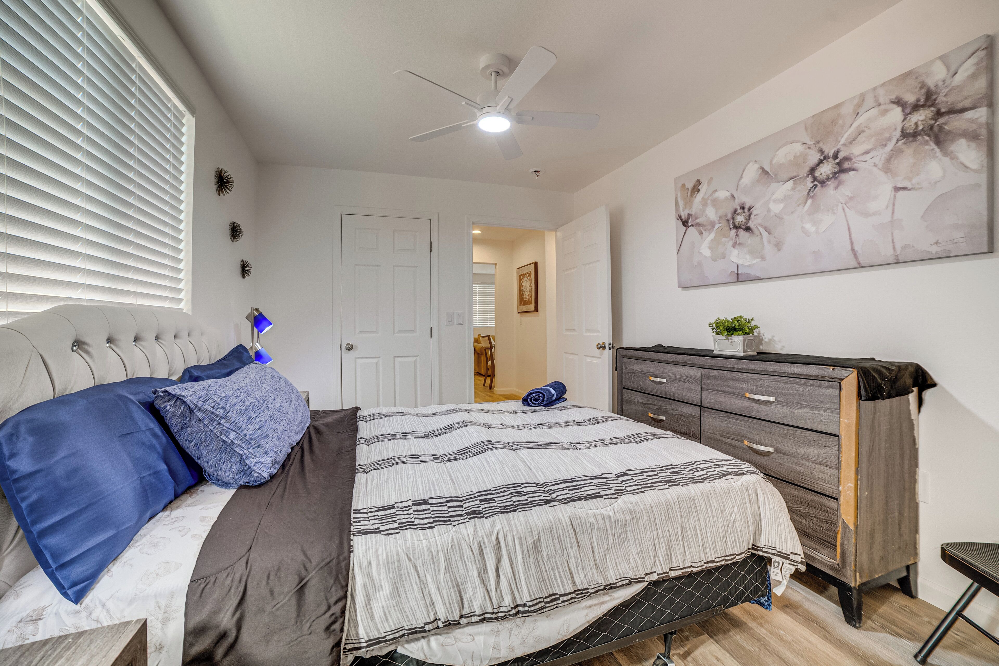 Een slaapkamer met een bed, een dressoir, een plafondventilator en een schilderij aan de muur.
