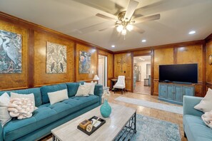 A spacious living room with a teal sofa, wooden paneling, a ceiling fan, and a flat-screen TV. - Group Getaway w/ Private Yard in Marietta (Marietta)