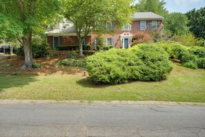 A two-story brick house with a front porch, surrounded by well-maintained lawns and trees. - Group Getaway w/ Private Yard in Marietta (Marietta)