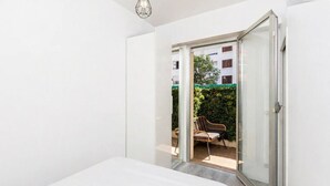 Een slaapkamer met een bed en een schuifdeur die leidt naar een buitenruimte met een stoel en een tafel.