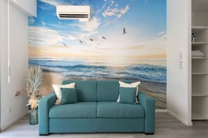 A teal sofa with white cushions in a room with a mural of a beach scene. - Maupassant Terrace | 2 min from the beach (Antibes)