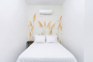 Ein Schlafzimmer mit einem Bett, weißer Bettwäsche, einem Nachttisch und einer Wandklimaanlage.