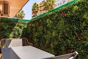 An outdoor seating area with a table and chairs, surrounded by a lush green wall with red flowers. - Maupassant Terrace | 2 min from the beach (Antibes)