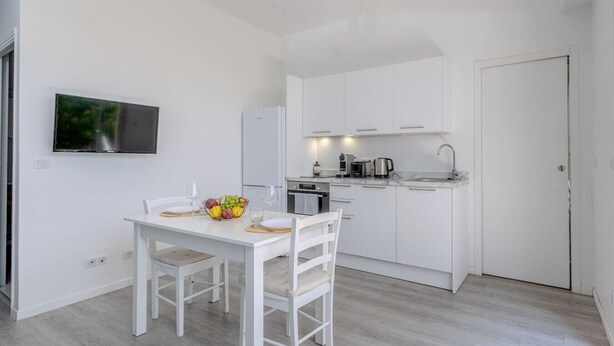 Een compacte keuken met witte kastjes, een eettafel met stoelen en een fruitschaal op tafel.