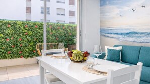 Een eetruimte met een tafel gedekt voor twee personen, een schaal fruit en een schilderij van een strand.