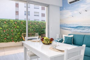A dining area with a table set for two, a bowl of fruit, and a painting of a beach scene. - Maupassant Terrace | 2 min from the beach (Antibes)