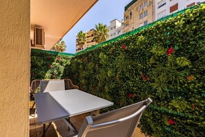 Ein Sitzbereich im Freien mit Tisch und Stühlen, umgeben von einer grünen Hecke mit roten Blüten.