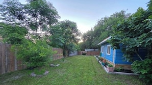 Ein Garten mit Holzzaun, einem kleinen Baum und einem blauen Haus.