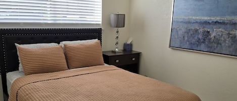 A bedroom with a bed, a nightstand, a lamp, a ceiling fan, and a painting on the wall.