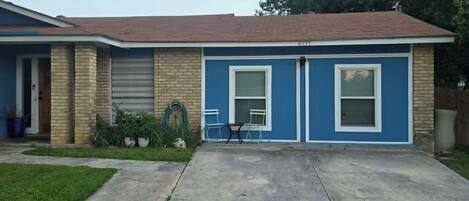 A residential house with a garage, a front door, and a small patio area with two chairs and a table.