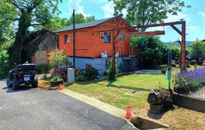 A rustic cabin with a red exterior, a wooden porch, and a small garden with flowers and a bird bath. - Beautiful home in Ludbreg with sauna (Ludbreg)