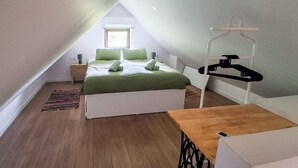 Un dormitorio con techo inclinado, una cama con ropa de cama verde, una mesita de noche con lámpara y un aparador de madera.