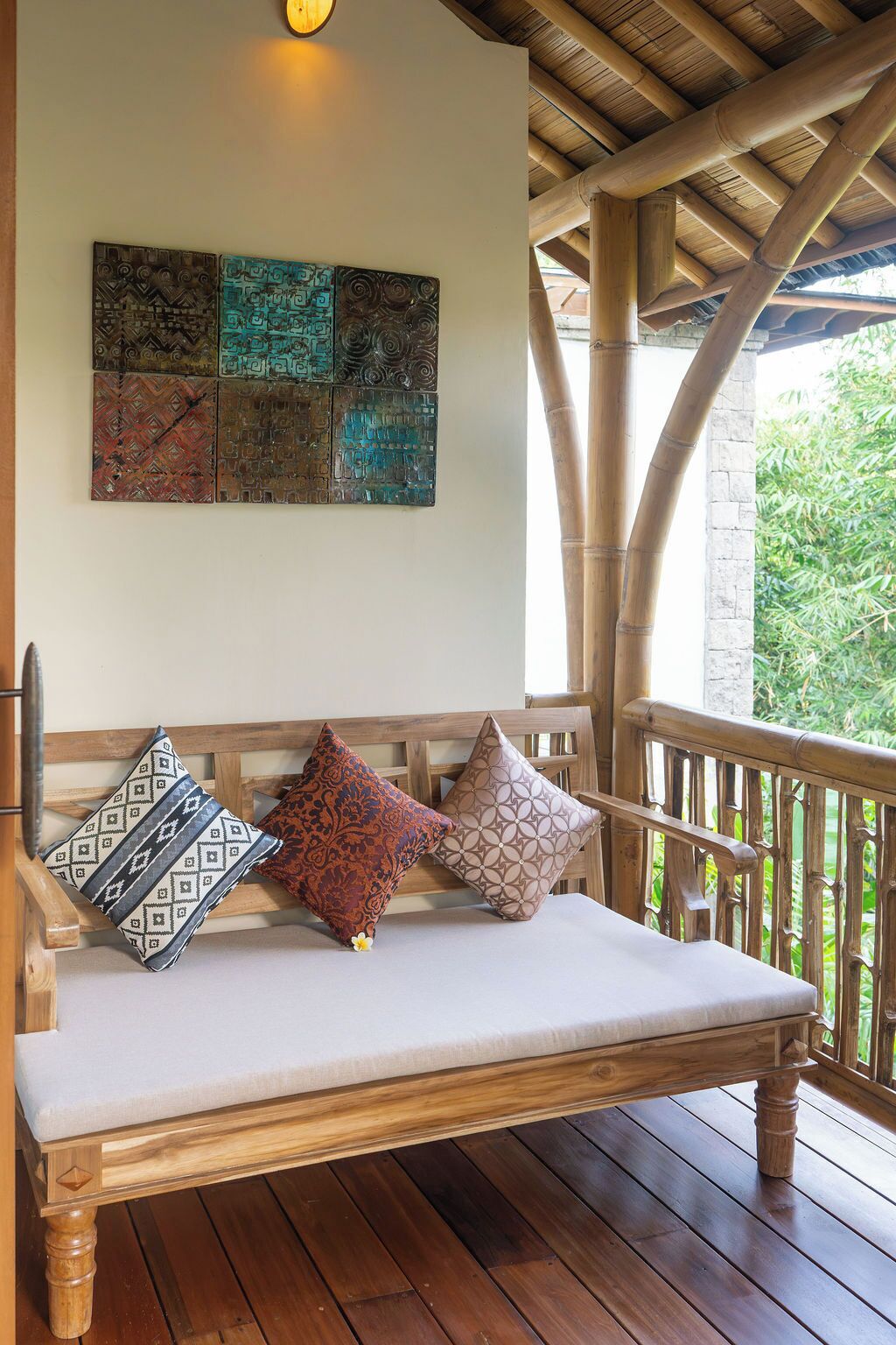 Un banco de madera con cojines, techo de bambú y una pared decorada con motivos.