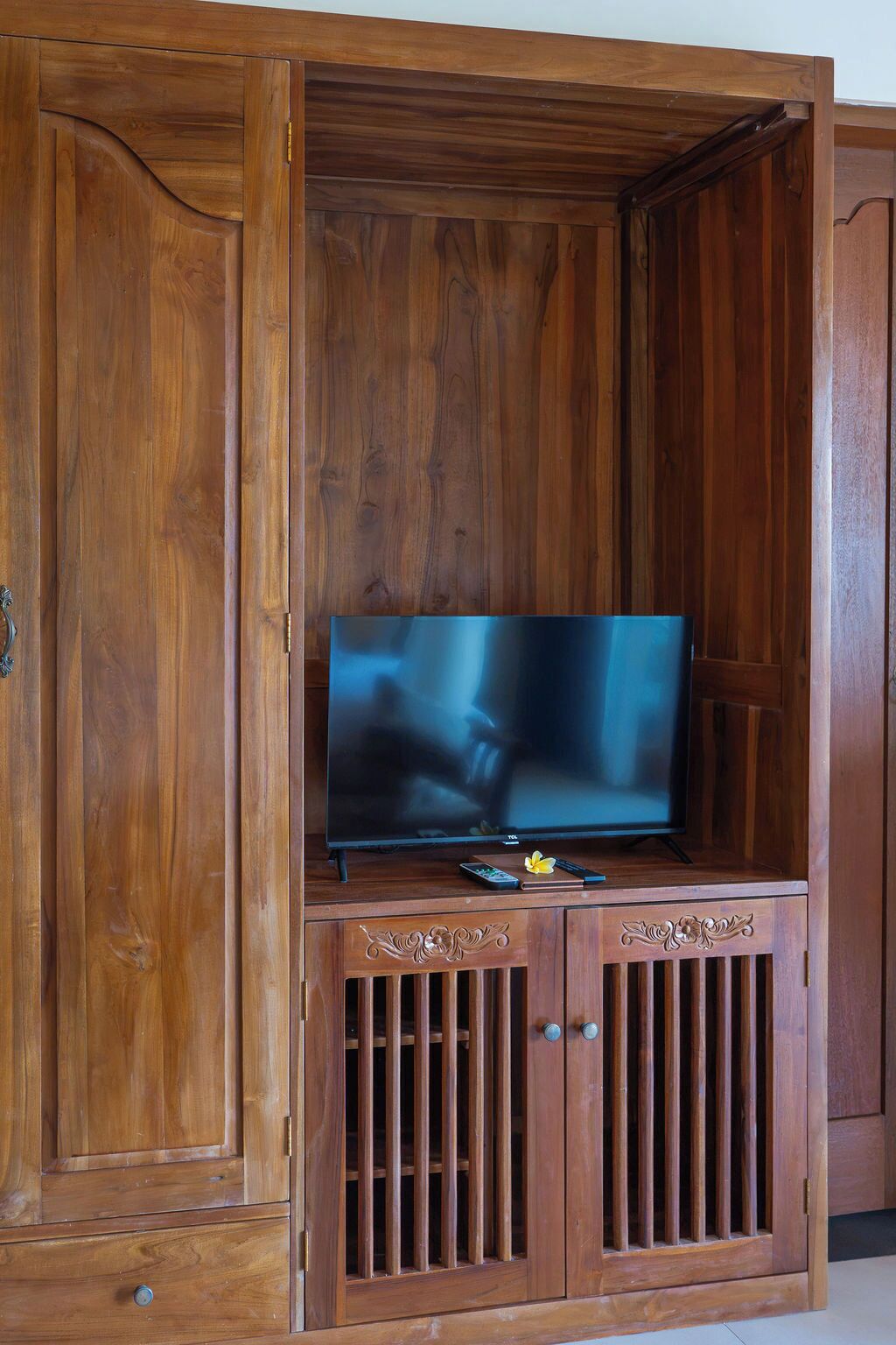 Un meuble de rangement en bois pour appareils multimédias, comprenant un téléviseur à écran plat, une télécommande et des éléments décoratifs.